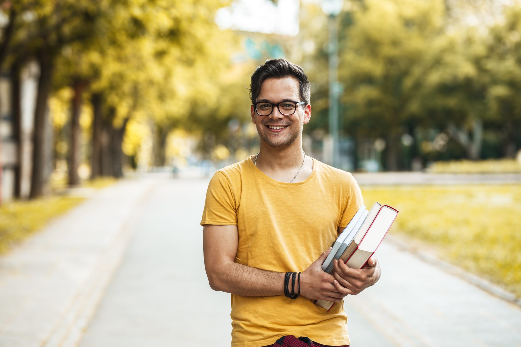 Young male student standing at the college yard.He holding a boo