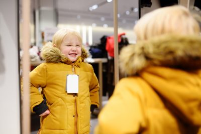 Cute little boy trying new coat during shopping. Fashion warm clothes for fall or winter. Kid/child in fitting room or in shopping center/mall