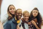 Close up of four happy teenage friends taking selfie outdoors. Girls piggy riding on the boys while taking a selfie outdoors.