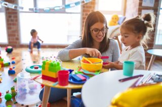 Young teacher and toddlers playing on the table with lots of toys at kindergarten