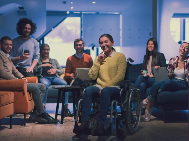 Portrait of businesswoman wheelchair user in front of her diverse business team in a modern open space coworking office space.