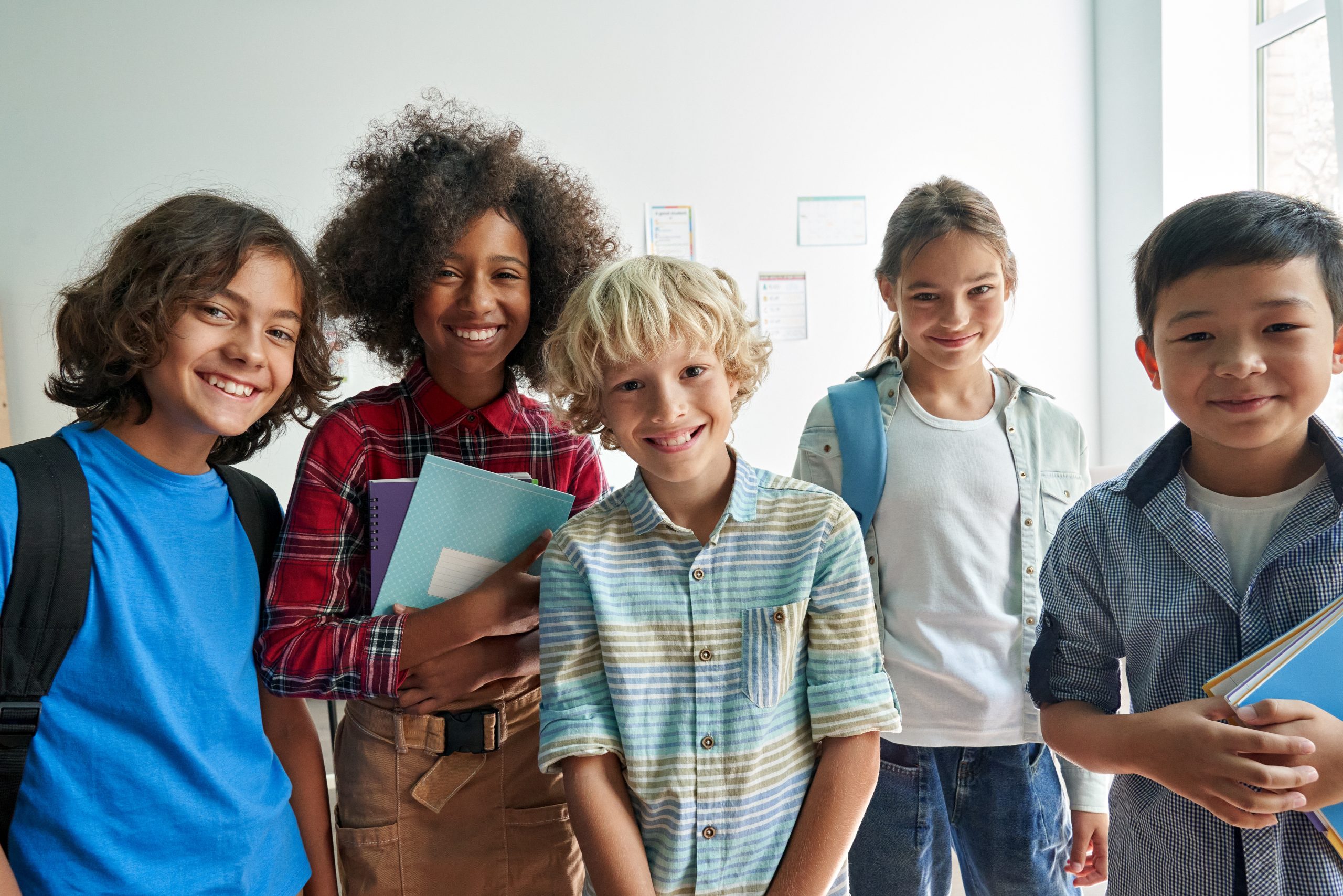 Happy diverse junior school students children group looking at camera standing in classroom. Smiling multiethnic cool kids boys and girls friends posing for group portrait together.
