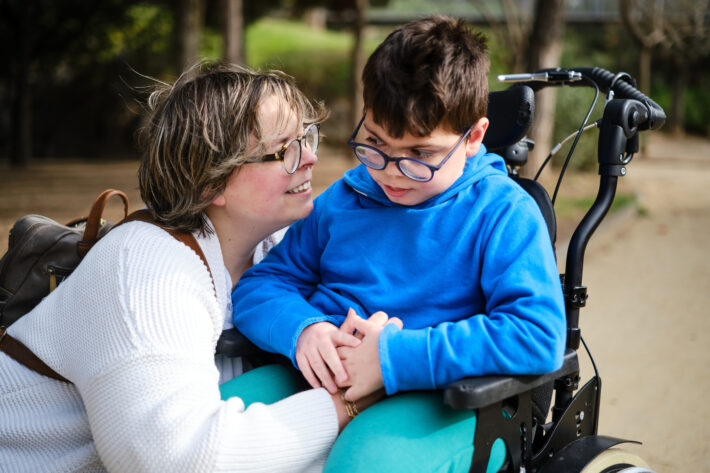 Boy with a disability using a wheelchair enjoying a walk outdoors with his mother.