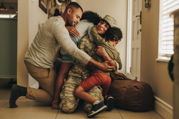 Happy military homecoming. Female soldier reuniting with her husband and children after serving in the army. Cheerful servicewoman embracing her family after returning home from deployment.