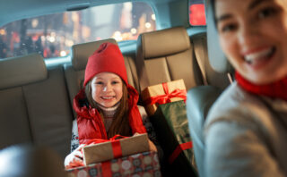 Woman and her child holding presents and delivering them on car to home. Holidays concept. Time of Christmas Eve.